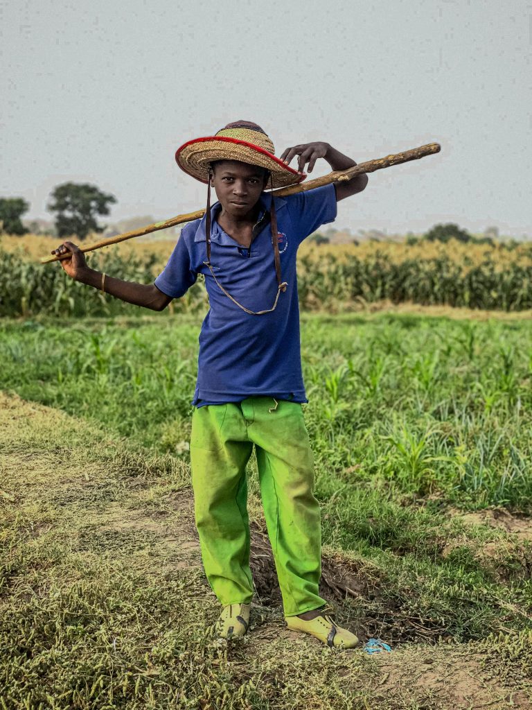 Portrait of a young farmer with a straw hat standing in a lush field in Kaduna South, Nigeria.