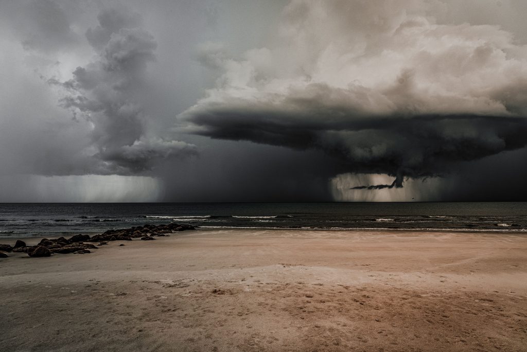 Dark storm clouds gather menacingly over a deserted beach by the ocean.