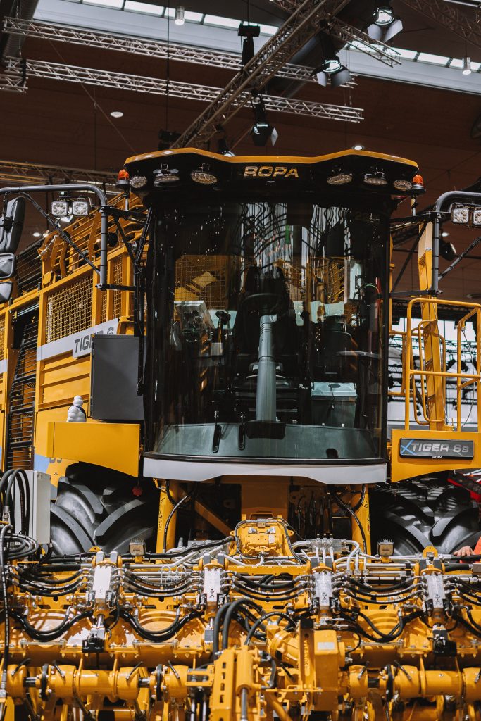 Showcase of a yellow modern harvester displayed indoors at an agricultural exhibition.