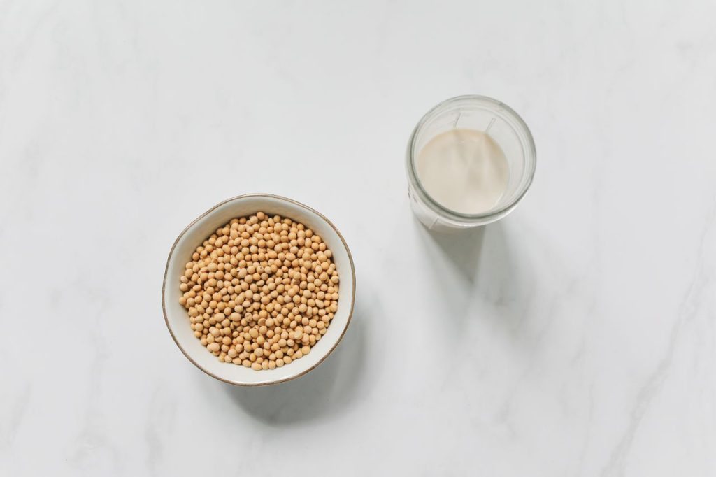 Bowl of soybeans and a glass of soy milk placed on white marble surface.